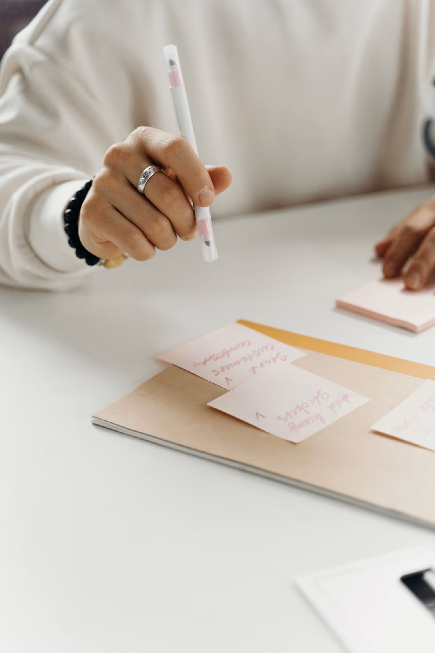 Nahaufnahme einer Hand, die einen Stift hält und auf rosafarbene Haftnotizen zeigt.