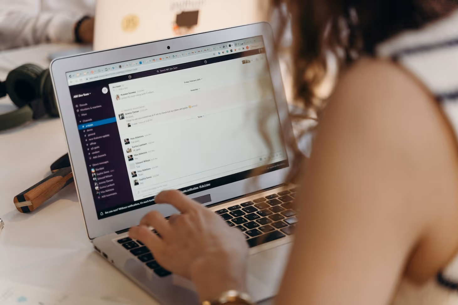Laptop-Bildschirm mit geöffneter Slack-Unterhaltung in einem Arbeitschat, im Vordergrund die Hand einer Person auf der Tastatur.